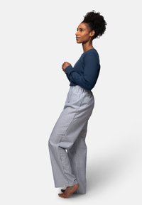 Navy top met lange mouwen, gecombineerd met hoog getailleerde, lichtblauwe en witte gestreepte wijde broek. Model staat blootvoets en toont een losse pasvorm.