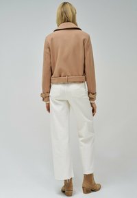 Chaqueta beige con solapas anchas, cinturón en la cintura y puños abotonados, combinada con pantalones de pierna ancha blancos y botines beige. Textura suave.