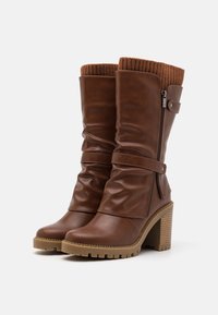 Brown faux leather knee-high boots with a ribbed knit cuff, a side zipper, and a chunky, textured heel. Features a slouched design and strap detail.