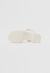 Sandale blanche à talon, dotée d'une semelle texturée, de fines sangles et d'une boucle dorée. Le talon a une forme bloc et une finition lisse et mate.