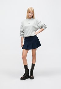 Γκρι φαρδιά μπλούζα φούτερ με κείμενο, σκούρα μπλε φούστα με πιέτες, σκούρες κάλτσες και μαύρα αρβυλάκια με κορδόνια. Απλός και καθημερινός σχεδιασμός.