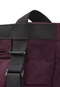 Burgundy fabric bag with black webbing straps, featuring a sturdy buckle and reinforced stitching on the handle area for added durability.