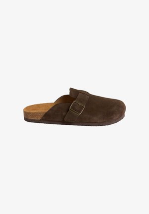Scarpa mocassino in camoscio marrone con punta arrotondata, plantare in sughero e fibbia metallica regolabile sulla fascia superiore. Superficie strutturata e suola piatta.