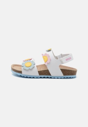 Sandales blanches avec des accents en forme de fleur en rose, jaune et bleu. Semelle en liège avec une semelle en caoutchouc bleu clair et une sangle réglable.