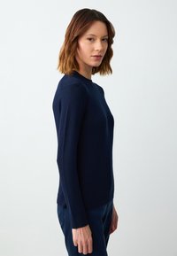 Granatowy sweter z dzianiny z okrągłym dekoltem, długimi rękawami oraz ściągaczami przy mankietach i na dole. Gładka tekstura i dopasowany krój.