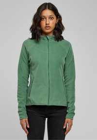 Zöld polár cipzáras pulóver magas gallérral, raglán ujjakkal és oldalzsebekkel, sima textúrával és testhezálló kialakítással.