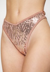 Parte de baixo de biquíni em rosa claro com padrão de zebra. Apresenta uma cintura em formato V e um detalhe decorativo de metal no quadril.