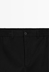 Zwarte broek met een elastiche tailleband, voorzien van een knoopsluiting en een gladde textuur. Geen zichtbare patronen of accenten.