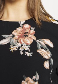 Top floreale nero con grandi motivi di fiori pesco e crema, che presenta foglie e piccoli fiori bianchi. Tessuto morbido con una finitura texturizzata.