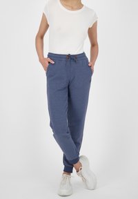 Bomullsmixade navy joggers med elastisk midja, dragsko detalj och ribbade fållar. Bärs med en vit åtsittande t-shirt och sneakers.