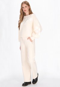 Creme strikket sweater med blomsterbroderi, parret med creme lige ben bukser og sorte træsko. Blød tekstur og afslappet pasform.