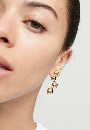 Pendientes de oro con tres formas esféricas de diferentes tamaños, con una superficie lisa y reflectante, colgando de un botón.