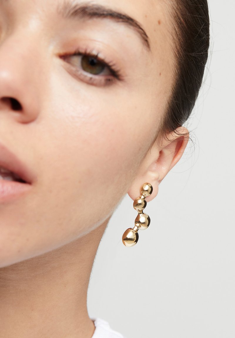 Boucles d'oreilles en or composées de trois sphères de tailles différentes, à surface lisse et réfléchissante, suspendues à une tige.