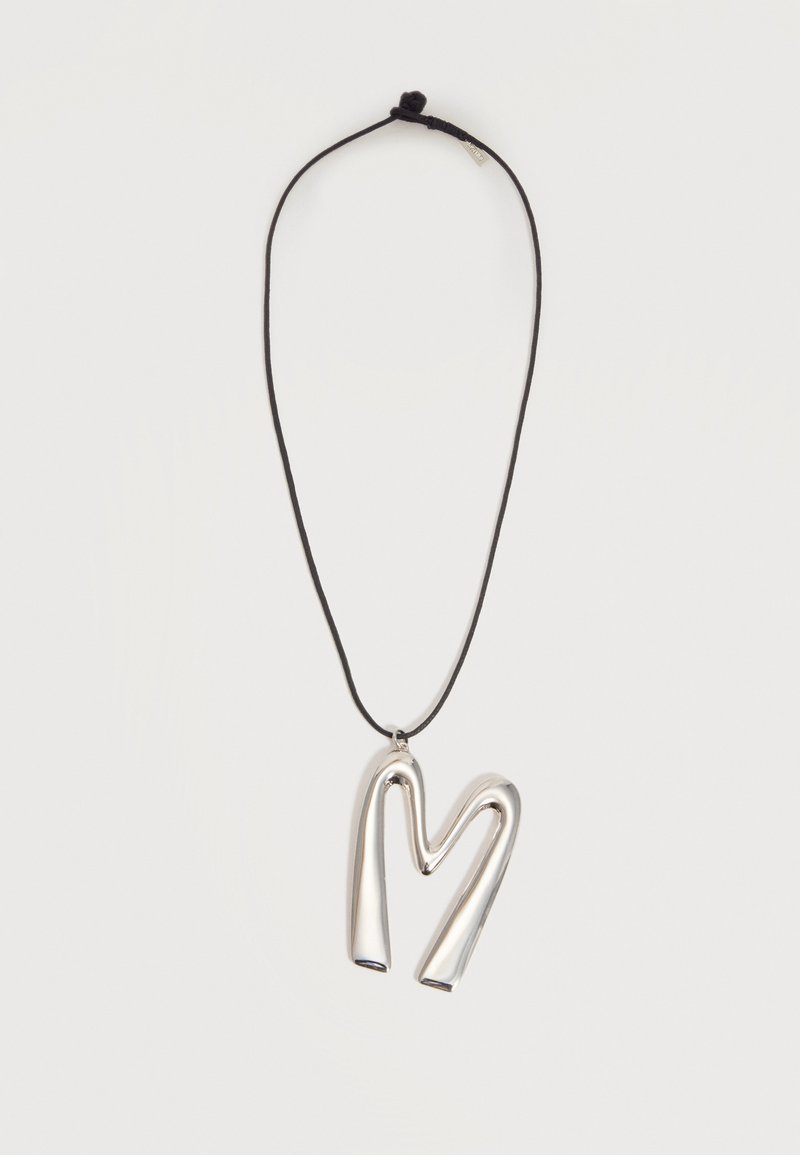 Collier à cordon noir avec un pendentif argenté brillant en forme de lettre "M" abstraite et arrondie sur un fond blanc uni.