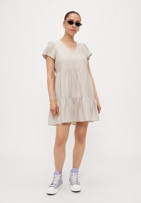 Φωτεινό μπεζ φόρεμα με κοντά φουσκωτά μανίκια, v-λαιμόκοψη, σχεδίαση με επίπεδα και υφασμάτινη υφή. Συνδυάζεται με παγωμένο μωβ αθλητικά παπούτσια υψηλής κορυφής.