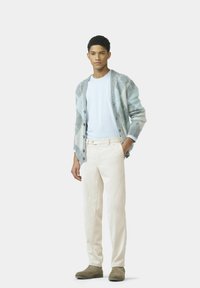 Hellblauer Cardigan mit Rautenmuster, Knopfleiste, kombiniert mit beigen Cordhosen und grauen Stiefeln, darunter ein schlichtes weißes T-Shirt.