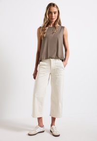 Top senza maniche di un marrone chiaro abbinato a pantaloni larghi color avorio con tasche applicate e sneaker crema con accenti grigi.
