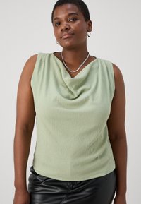 Top sin mangas de color verde menta con escote de drapeado, textura acanalada y un corte holgado. Combinado con una falda de cuero negra y un collar de plata.