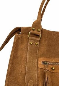 Sac à main en suède marron avec poignée tressée, poche zippée à l'avant avec tirette à frange, et détails en rivets en laiton et en boucle.