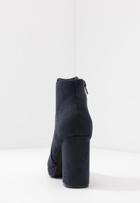 Navy suede ankle boot with a round toe and a tall block heel. Features a side zipper and smooth texture.