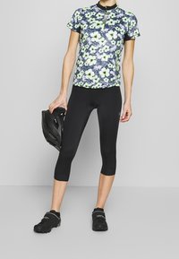 Strój rowerowy składający się z lekkiej, krótkosleeve'owej koszulki z kwiatowym wzorem w odcieniach niebieskiego i zielonego, zestawionej z czarnymi legginsami do połowy łydki oraz czarnymi butami rowerowymi.