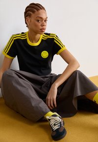 Black T-shirt with yellow accents and a smiley face graphic, paired with a gray skirt. Yellow socks and sneakers complete the outfit.