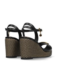 Czarne skórzane sandały na koturnie z teksturowaną, plecioną podeszwą i złotym akcentem na pasku wokół kostki. Otwarty design palców.