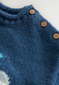 Blue knitted garment with three brown round buttons along the shoulder seam on a light background.