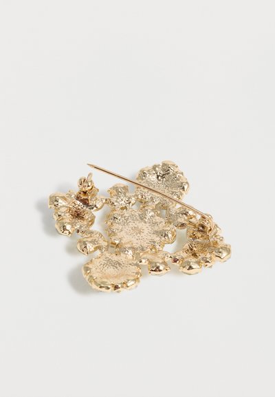 Καρφίτσα από μέταλλο με χρυσαφί τόνο σε σχήμα υφασματωμένων συστάδων λουλουδιών με κούμπωμα καρφίτσας στην πίσω πλευρά.