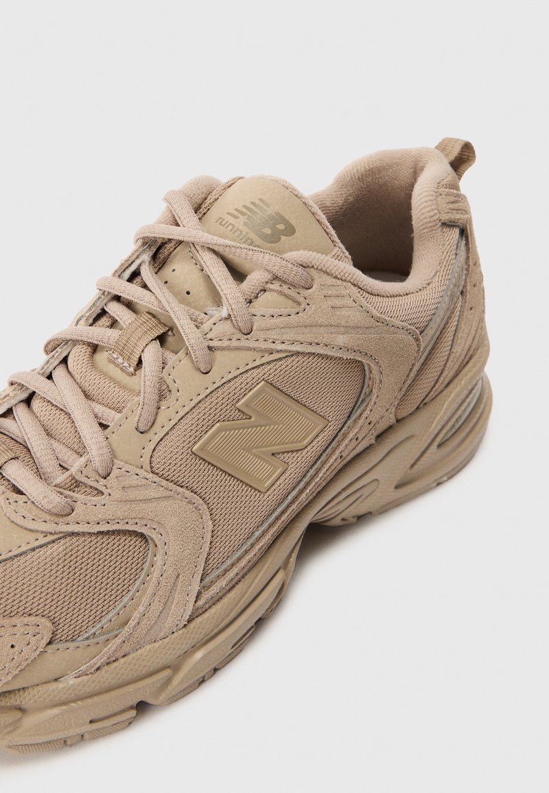 Beige Sport Schuh aus Netz- und Wildledermaterialien, runde Zehenpartie, strukturierte Akzente und großes 'N'-Logo an der Seite.