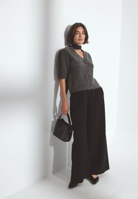 Pelēks adīts kardigans ar īsām piedurknēm un pogām, kombinēts ar platām melnām biksēm. Aksesuāri: mazs melns rokassoma un norādītas kurpes.