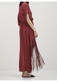 Red maxi dress with short sleeves, gathered waist, and side fringe detailing. Made of lightweight fabric with a smooth texture.