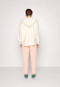 Krémová mikina s švem na zádech a šňůrkou, spárovaná s volnými broskvovými kalhotami a teniskami s zelenými akcenty. Minimalistický design; měkké textury.