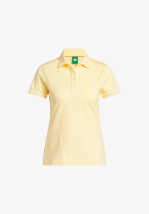 Žlté polo tričko s krátkym rukávom, tromi gombíkmi, golierom, malým logom Adidas na hrudi a zelenou štítkou vo vnútri goliera.