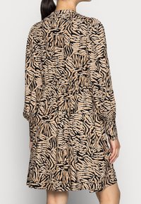 Långärmad klänning i svart tyg med ett beige abstrakt djurtryck, med en smal midja och en knäppt krage. Strukturerad yta.