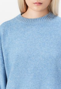 Lyseblå genser laget av mykt, teksturert stoff. Har en ribbestrikket rund hals og en avslappet passform for komfort.