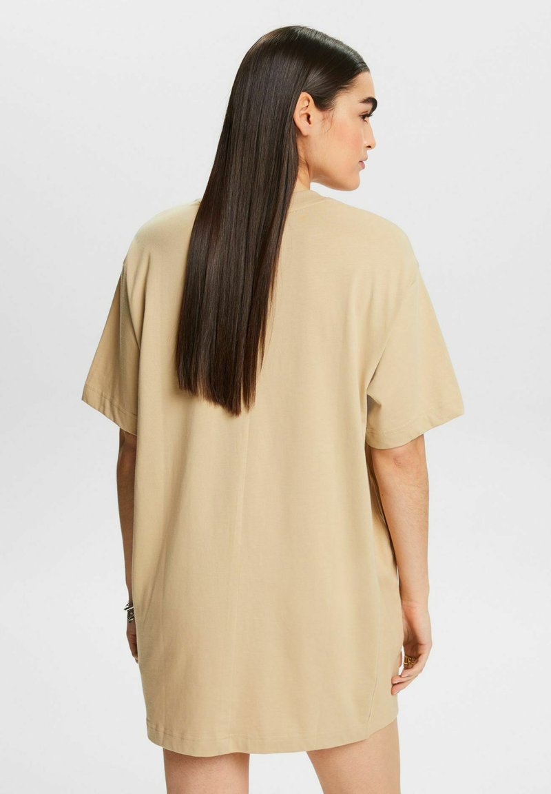 Beżowy oversize t-shirt z krótkimi rękawami, miękka tkanina, luźny krój i prosty dół, przedstawiony z tyłu, z widocznymi długimi włosami.