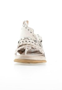 Sandale en cuir blanc avec des clous argentés, des brides tressées et une semelle en bois plate, vue de face sur un fond blanc.