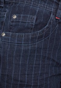 Tmavě modré džíny z denimu se jemným vertikálním pruhovaným vzorem, se stříbrnými doplňky a malou přední kapsou. Jemná textura.