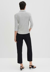 Camicia colletto a righe grigie e bianche con maniche a tre quarti, abbinata a pantaloni neri a sigaretta e sandali neri con tacco.