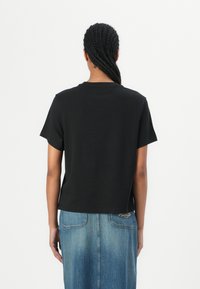 Svart t-shirt med kort ärm och rund halsringning, tillverkad av mjuk bomull, visad bakifrån, i kombination med en blå denimkjol.