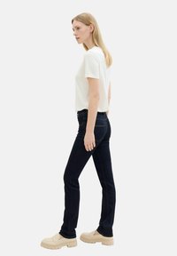 Vaqueros azul oscuro combinados con una camiseta blanca y zapatos gruesos beige. Los vaqueros tienen bolsillos estándar y detalles de costura en contraste.