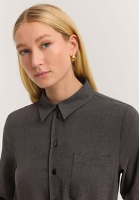 Graues Button-Up-Hemd mit Kragen, kurzen Ärmeln, Brusttasche und schwarzen Knöpfen. Glatte Textur mit feinen Musterdetails.