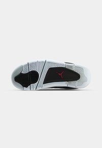Suela de zapatilla en blanco y negro con patrón de espiga, goma gris texturada y un acento de logo rojo sobre una superficie lisa.