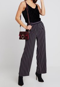 Top negro plisado con tirantes finos, combinado con pantalones de pierna ancha a rayas en tonos azul marino y rosa. Un bolso burdeos con estampado completa el conjunto.
