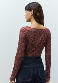 Lace lange mouw top in mauve, met bloemmotieven en een brede halslijn. Gecombineerd met hoge taille donkerdenim jeans.