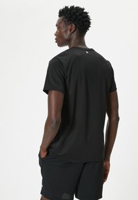 Camiseta deportiva negra hecha de tejido ligero, con mangas cortas y cuello redondo, acompañada de pantalones cortos negros. Sin logotipos visibles.