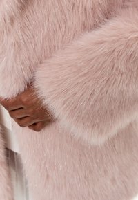 Lyserød faux fur beklædning med lange, bløde fibre og subtil glans, med brede manchetter og en glat overflade. Hånd krammet mod stoffet.