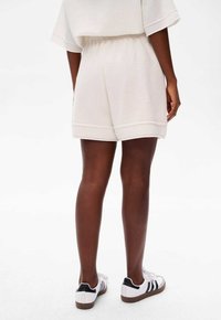 Witte gebreide shorts met een elastische tailleband, voorzien van een zachte textuur en opgerolde manchetten. Draagt met witte en zwarte sneakers.