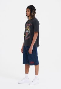 Black graphic t-shirt with a tiger design, blue denim shorts with red embroidered text, and white sneakers.